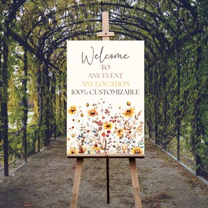 May include: A wooden easel displays a welcome sign with floral watercolor art. The sign reads "Welcome to Any Event Any Location 100% Customizable" in elegant script. The floral design features yellow sunflowers and other wildflowers.