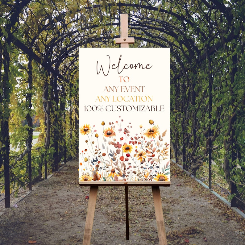 May include: A wooden easel displays a welcome sign with floral watercolor art. The sign reads "Welcome to Any Event Any Location 100% Customizable" in elegant script. The floral design features yellow sunflowers and other wildflowers.