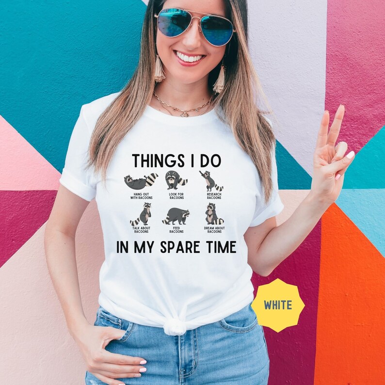 May include: White t-shirt featuring a graphic of raccoons and the text "Things I do in my spare time". The graphic depicts raccoons engaged in various activities, such as hanging out, looking for raccoons, researching raccoons, talking about raccoons, feeding raccoons, and dreaming about raccoons.