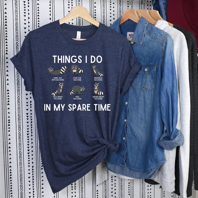 May include: A navy blue t-shirt with a white graphic of raccoons and the text "Things I do in my spare time". The graphic shows raccoons hanging out, looking for raccoons, researching raccoons, talking about raccoons, feeding raccoons, and dreaming about raccoons.