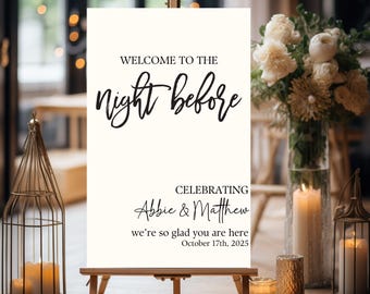 May include: A cream-colored welcome sign on a wooden easel. The sign reads "WELCOME TO THE night before CELEBRATING Abbie & Matthew we're so glad you are here October 17th, 2025" in elegant black script. The scene includes candles and floral arrangements.
