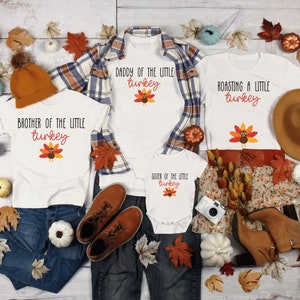 May include: A set of four white t-shirts with Thanksgiving-themed graphics. The shirts feature a turkey design and text that reads "Brother of the Little Turkey", "Daddy of the Little Turkey", "Roasting a Little Turkey", and "Sister of the Little Turkey".
