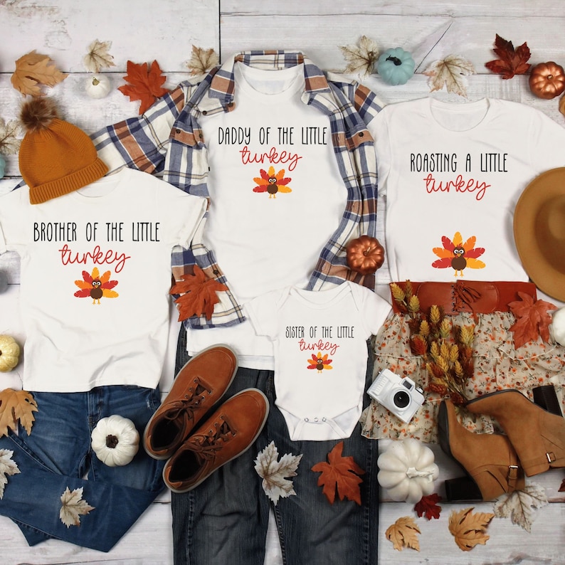 May include: A set of four white t-shirts with Thanksgiving-themed graphics. The shirts feature a turkey design and text that reads "Brother of the Little Turkey", "Daddy of the Little Turkey", "Roasting a Little Turkey", and "Sister of the Little Turkey".