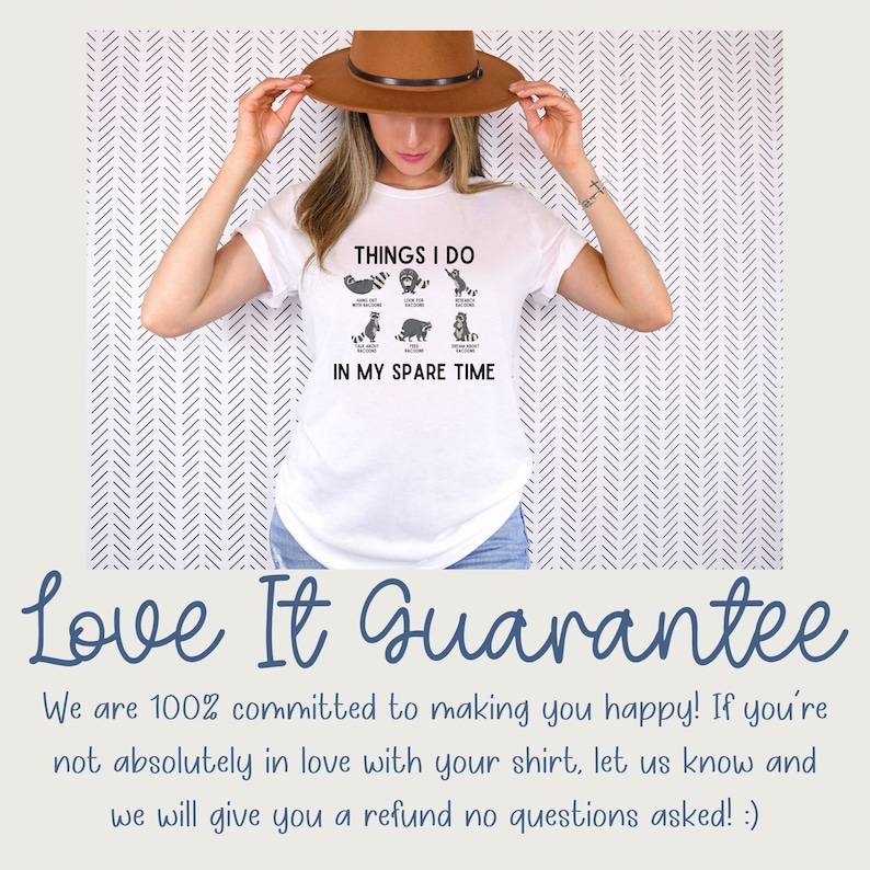 May include: White t-shirt featuring a graphic of a raccoon doing various activities with the text "Things I do in my spare time". The model is wearing a brown hat and holding the shirt in front of her.