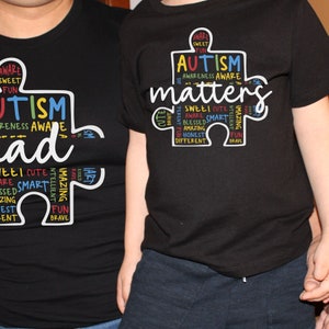 May include: Two black t-shirts with a puzzle piece design. The adult shirt says "Autism Dad" and the child's shirt says "Autism Matters". Both shirts have the words "aware, sweet, fun, blessed, smart, amazing, honest, different, brave, cute, intelligent" written on the puzzle piece.