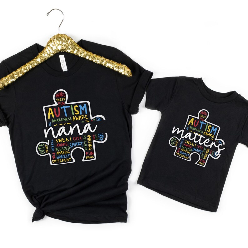May include: Two black t-shirts with a puzzle piece design. The larger shirt says "Autism Awareness Aware nana" and the smaller shirt says "Autism Matters". Both shirts have colorful text around the puzzle piece.
