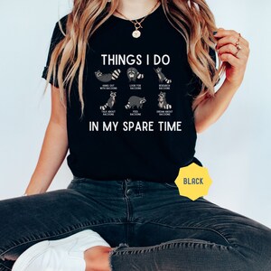 May include: Black t-shirt with the text "THINGS I DO" and illustrations of raccoons doing various activities. The text below the illustrations reads "IN MY SPARE TIME".