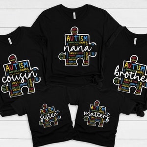 May include: Five black t-shirts with a white puzzle piece design. The puzzle piece is filled with colorful text that says "Autism Awareness" and includes words like "sweet", "cute", "amazing", "brave", "honest", and "different". The shirts have different text on them, including "nana", "cousin", "sister", "brother", and "matters".