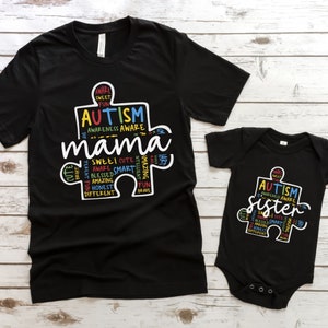 May include: Black t-shirt and bodysuit with a white puzzle piece design. The puzzle piece is filled with colorful words related to autism awareness, including "Autism", "Mama", and "Sister".