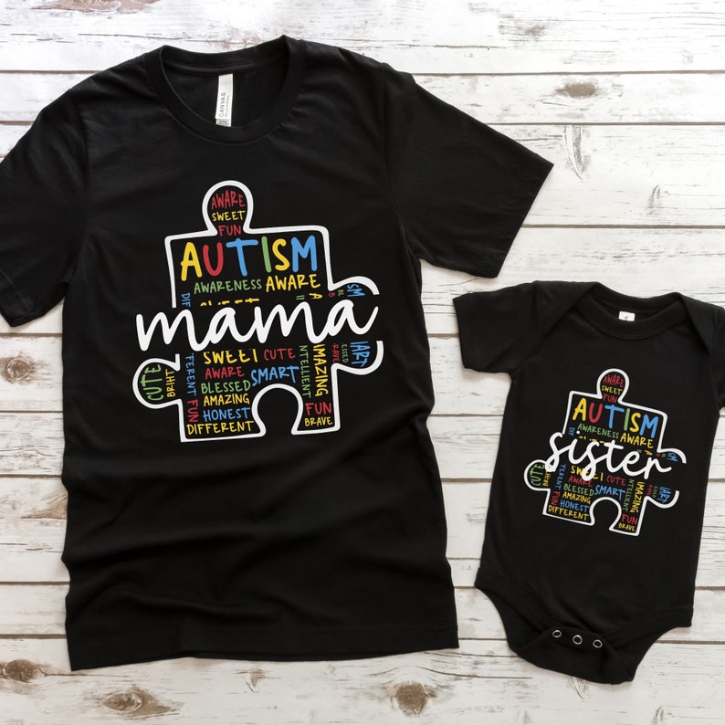 May include: Black t-shirt and bodysuit with a white puzzle piece design. The puzzle piece is filled with colorful words related to autism awareness, including "Autism", "Mama", and "Sister".