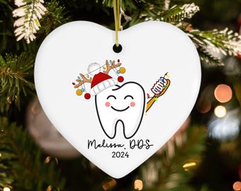 May include: White heart-shaped Christmas ornament with a cartoon tooth wearing a Santa hat and holding a toothbrush. The ornament says "Melissa, DDS 2024".