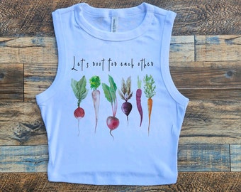 May include: White sleeveless crop top with the text "Let's root for each other" and a watercolour illustration of various vegetables, including carrots, radishes, and beets.