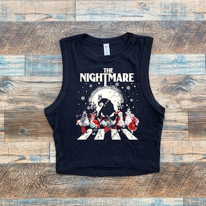 Puede incluir: Top corto sin mangas negro con el texto "THE NIGHTMARE" sobre un gr&aacute;fico de personajes de Pesadilla antes de Navidad cruzando una calle. El dise&ntilde;o presenta una luna llena y copos de nieve.