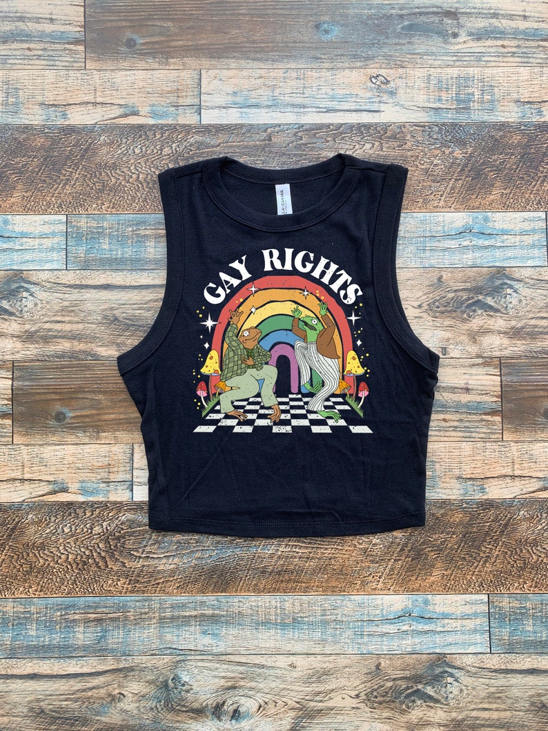 May include: Black crop top with the words "GAY RIGHTS" in white arched over a rainbow graphic. The graphic features two frog-like characters on a checkered floor. The top has a crew neck and sleeveless design.