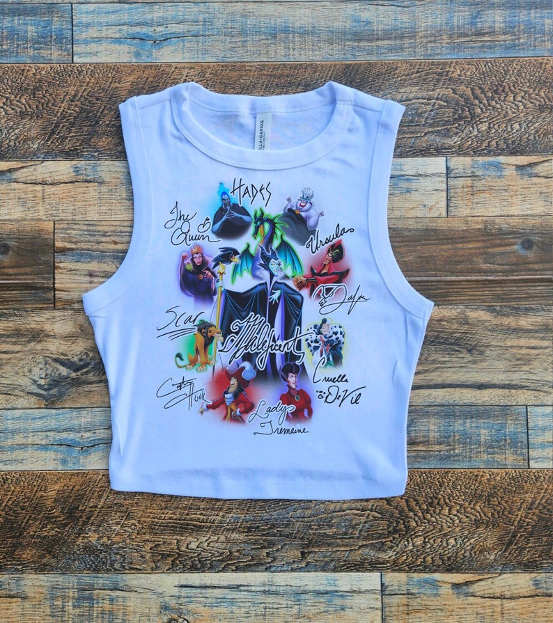 May include: White sleeveless crop top with a colorful graphic print of Disney villains, including Maleficent, Ursula, Cruella de Vil, and Scar. The villains are depicted in their signature poses and surrounded by their respective symbols. The text "Villainous" is printed in a bold font below the image.