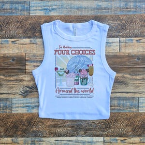 May include: White sleeveless crop top with the text "I'm Making Pour Choices Around the World." The graphic features colorful cocktails and a blue sphere design. The shirt is made of a soft material.
