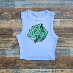 May include: White sleeveless crop top with a green shamrock and lightning bolt graphic that says "Lucky" in a retro font.