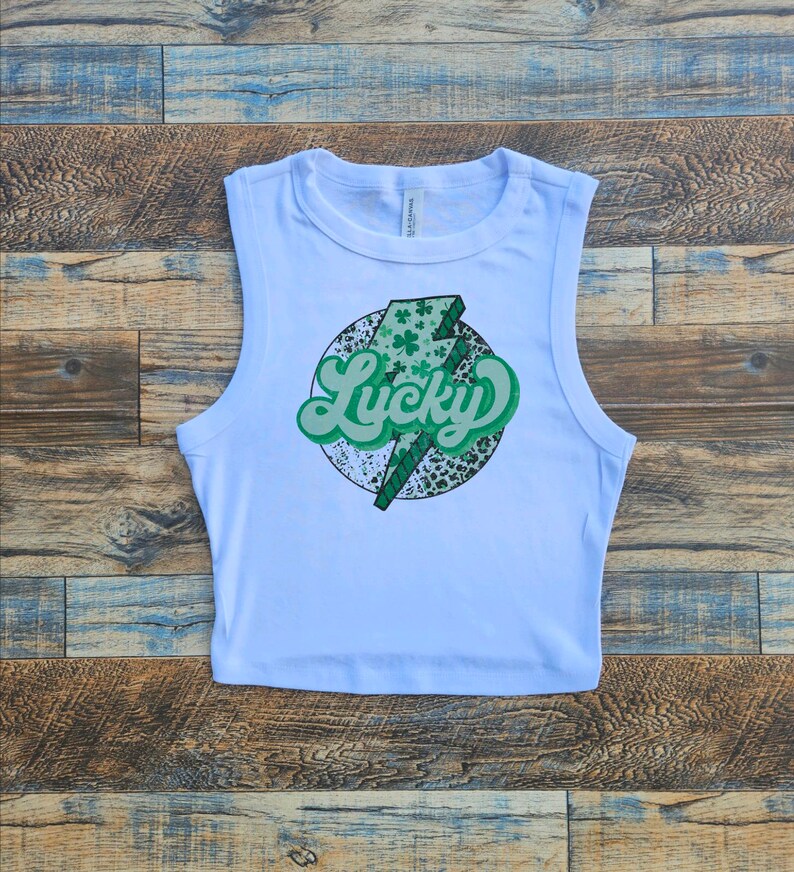 May include: White sleeveless crop top with a green shamrock and lightning bolt graphic that says "Lucky" in a retro font.