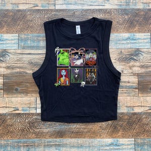 May include: Black sleeveless crop top featuring a colorful graphic of postage stamps with characters from a popular animated movie. The stamps include images of a green monster, a skeleton, and a rag doll.