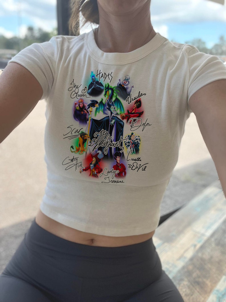 May include: White crop top with a graphic print of Disney villains, including Maleficent, Ursula, Cruella de Vil, and Hades. The villains are depicted in their signature poses and surrounded by their names in a handwritten font.