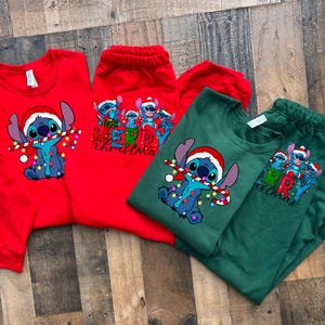 May include: Red and green Christmas themed shirts featuring Stitch from Lilo & Stitch. The red shirt has a group of Stitch characters with the text "Merry Christmas". The green shirt has a single Stitch character holding a candy cane and lights with the text "Merry Christmas".