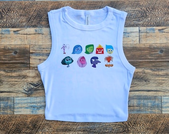 May include: White sleeveless crop top with a graphic print of the characters from the movie Inside Out. The characters include Joy, Sadness, Anger, Fear, and Disgust.