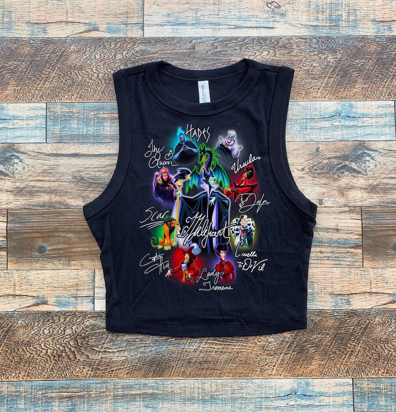 May include: Black sleeveless crop top with a graphic print of Disney villains including Maleficent, Ursula, Cruella de Vil, and Hades. The villains are depicted in their signature poses and surrounded by their signature colors. The text "The Villains" is printed in white on the front of the shirt.