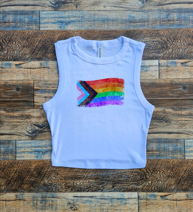 May include: White sleeveless crop top with a distressed print of a pride flag with black, brown, light blue, pink, white, green, light blue, and yellow stripes.