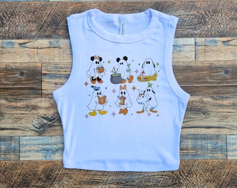 May include: White sleeveless crop top with a colorful print of cartoon ghosts dressed in Halloween costumes. The ghosts are holding candy, a cauldron, and a pumpkin.