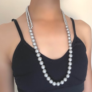 以下が含まれることがあります： ダブルの真珠のネックレス。シルバーの真珠が使用されています。ネックレスは、黒いタンクトップを着た人が着用しています。