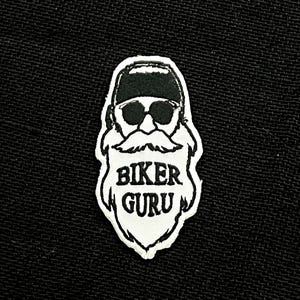Könnte beinhalten: Gestickter Aufnäher mit einem stilisierten Biker mit Sonnenbrille, Bart und Mütze. Der Text "BIKER GURU" ist fett und in Großbuchstaben dargestellt. Der Aufnäher ist weiß mit schwarzen Details und vor einem schwarzen Stoffhintergrund.