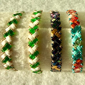 May include: Four beaded bracelets arranged in a row. The first is white and green, the second is green and white, the third is iridescent dark purple and gold, and the fourth features a mix of orange, turquoise, and red glass beads.