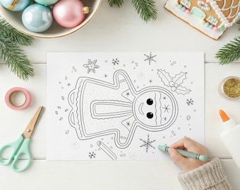 May include: A black and white gingerbread man coloring page with snowflakes and holly. A person is coloring the page with a green crayon. Christmas ornaments, a gingerbread house, and craft supplies are also visible.