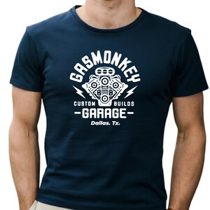 Pode incluir: Uma camiseta azul marinho com um gr&aacute;fico branco de um motor estilizado e o texto "Gas Monkey Custom Builds - Garage - Dallas, Tx."