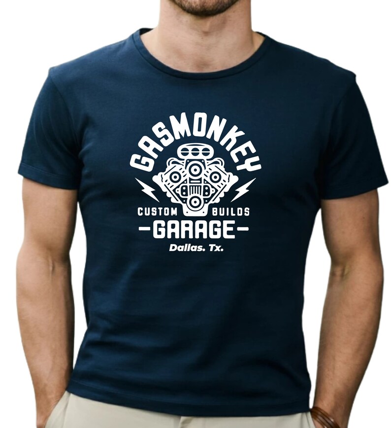 Pode incluir: Uma camiseta azul marinho com um gr&aacute;fico branco de um motor estilizado e o texto "Gas Monkey Custom Builds - Garage - Dallas, Tx."