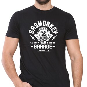 Pode incluir: Camiseta preta com um gr&aacute;fico branco de um motor estilizado com o texto "Gas Monkey Custom Builds - Garage - Dallas, Tx."