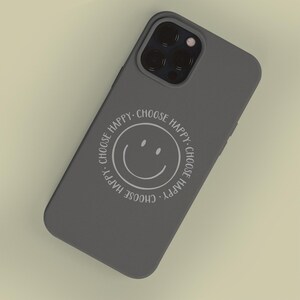 K&ouml;nnte beinhalten: Eine graue Handyh&uuml;lle mit einem wei&szlig;en Smiley und dem Text "Choose Happy", der sich um das Gesicht wiederholt.