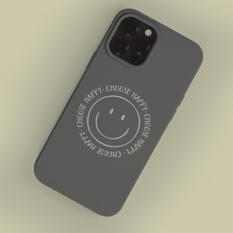 K&ouml;nnte beinhalten: Eine graue Handyh&uuml;lle mit einem wei&szlig;en Smiley und dem Text "Choose Happy", der sich um das Gesicht wiederholt.
