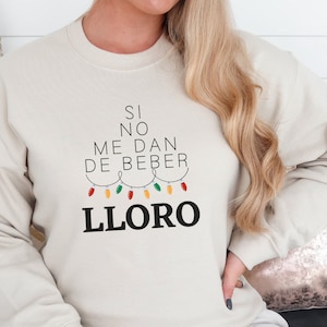 May include: A cream coloured sweatshirt with the text "Si no me dan de beber LLORO" and a string of Christmas lights.