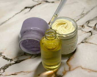 Op de afbeelding: Drie glazen potten met verschillende schoonheidsproducten. Een glazen pot met een gele vloeistof, een paarse pot met een paarse crème en een glazen pot met een witte crème.