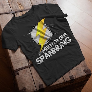 Könnte beinhalten: Schwarzes T-Shirt mit einem gelben Blitz-Motiv und dem Text "Meister der Spannung" in Weiß.