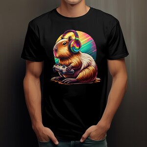 Könnte beinhalten: Ein schwarzes T-Shirt mit einem Aufdruck eines Capybaras, das Kopfhörer trägt und einen Videospielcontroller hält. Das Capybara ist braun und weiß vor einem bunten Hintergrund.