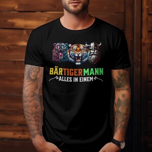 Könnte beinhalten: Schwarzes T-Shirt mit einem Aufdruck eines Bären, Tigers und Wikingers mit dem Text "Bärtigermann Alles in einem" in Regenbogenfarben.