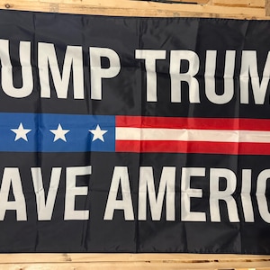 Può includere: Bandiera nera con testo bianco che recita "DUMP TRUMP SAVE AMERICA". La bandiera presenta una striscia blu con quattro stelle bianche e strisce rosse e bianche, che assomigliano a una bandiera americana stilizzata.