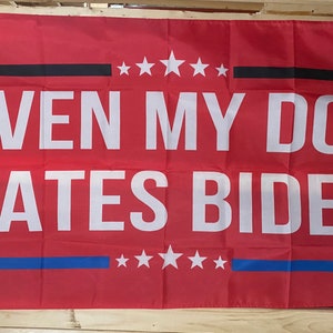 May include: A red flag with a black stripe and a blue stripe. The flag has white stars and the text "EVEN MY DOG HATES BIDEN".