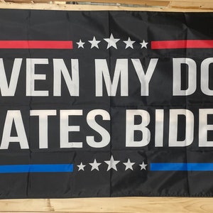 May include: Black flag with white text that reads "Even My Dog Hates Biden". The flag has red and blue stripes with white stars.