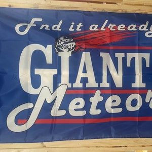May include: A blue flag with white text that reads "Find it already GIANT Meteor" with a red comet and a white moon in the upper left corner.
