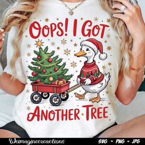 Könnte beinhalten: Cremefarbenes T-Shirt mit einem weihnachtlichen Motiv. Das Design zeigt eine Ente mit Weihnachtsmütze und Weihnachtspullover, die einen Wagen mit einem geschmückten Weihnachtsbaum zieht. Der Text lautet "Oops! I Got Another Tree."