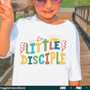 Könnte beinhalten: Ein weißes T-Shirt mit einer bunten Grafik, auf der "Little Disciple" mit einer Krone, Herzen, Sonne und Blitzen steht.