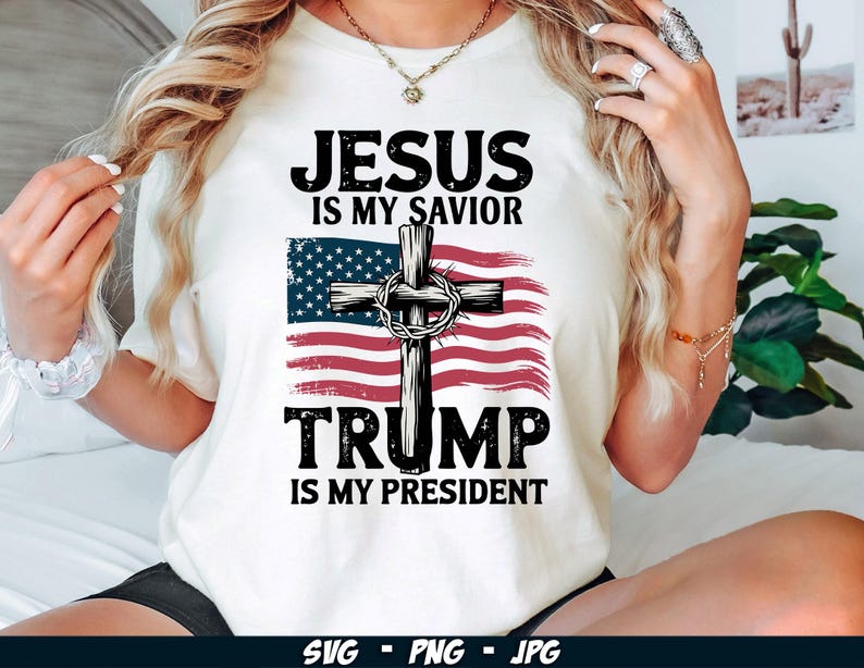 May include: White t-shirt with a red, white and blue American flag featuring a cross and the text "Jesus is my Saviour, Trump is my President".